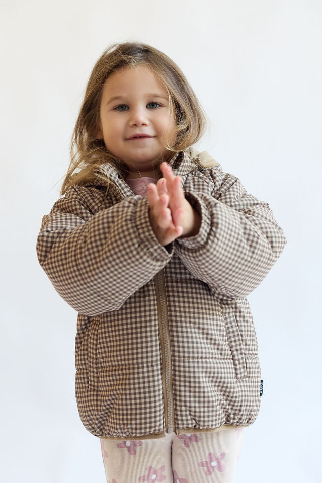 ילדה לובשת מעיל פאפר משובץ בגווני חום ושמנת עם קפוצ'ון ורוכסן קדמי – בינה & בינו