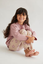 ילדה לובשת חליפת ריב עם חולצה ורודה ומכנסיים מתרחבים בגוון שמנת בהדפס פרחים ורודים – בינה & בינו
